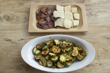 fried zucchini slices with cheese and salami platter on wooden table