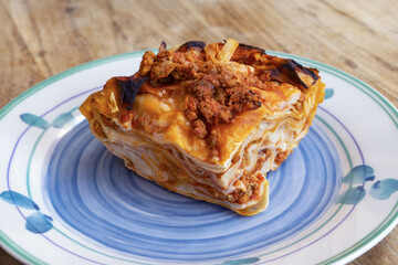
slice of layered lasagna with meat sauce on blue plate close up