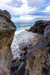 A dramatic view through the dark volcanic rocks of a secluded cove on the rugged coast of São Miguel, Azores, where the Atlantic waves crash onto a patch of black sand
