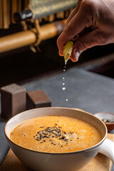Hand squeezing lime into curry soup bowl
