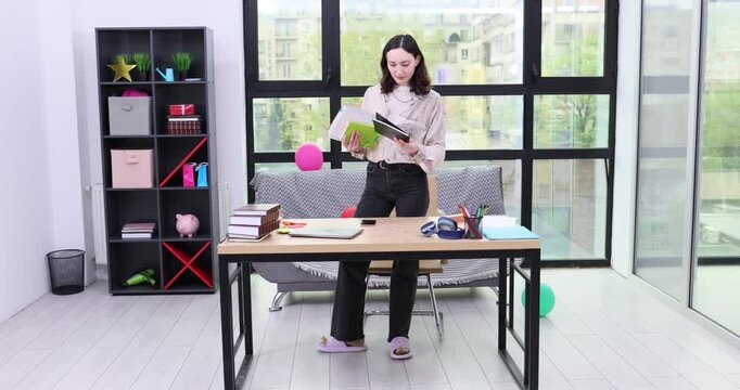 Woman in office stands at cluttered desk while sorting items. Woman secretary moves objects across table organizing workplace during busy day