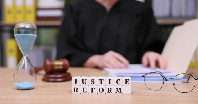 Advocates discuss change and justice in a bustling office setting with papers and an hourglass emphasizing timely reform efforts