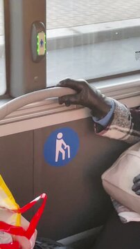 window seat with priority icon, gloved hand resting on rail beside colorful shopping bag, urban commute scene through moving. Vertical shot taken on mobile device.