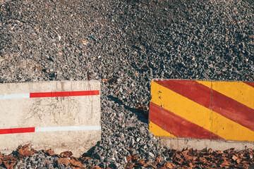 Red and yellow striped concrete barrier placed in front of a gravel pile on a road construction site.