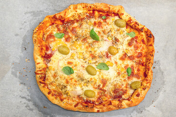 Fresh homemade pizza with melted cheese, olives, tomato sauce, and basil leaves on baking paper.