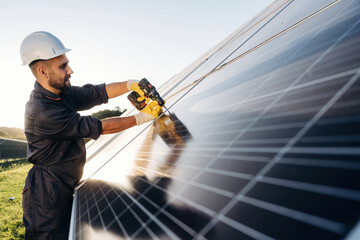 Yellow drill is in hands, installation process. Male solar engineer examining photovoltaic panels at a power station