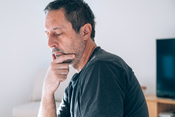 Authentic middle-aged caucasian man sitting in profile, hand on chin, looking deeply thoughtful and worried.
