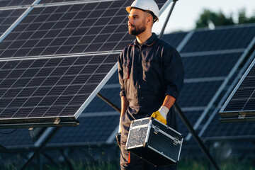 Ready for work, holding box with tools. Male solar engineer examining photovoltaic panels at a power station