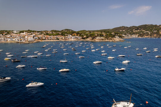 Aerial view of boats dot the deep blue sea near the white buildings of Calella de Palafrugell, creating a vibrant contrast of colors and textures, Calella de Palafrugell, Catalonia, Spain.
