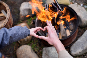 Child and adult palms showing heart sign against a burning fire in the backyard