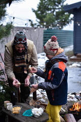 Father and son in winter clothes holding roasted marshmallow on stick with cookies in backyard