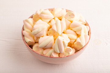 Orange and pink marshmallow in ceramic bowl on white wooden, side view, copy space