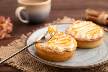 French lemon tart with meringue on brown wooden, linen textile, side view, close up, selective focus