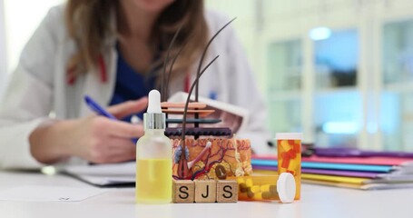 Wooden blocks spell letters SJS near skin model and medicine. Woman doctor writes notes about Stevens Johnson syndrome treatment at appointment