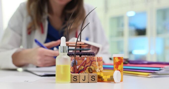 Wooden blocks spell letters SJS near skin model and medicine. Woman doctor writes notes about Stevens Johnson syndrome treatment at appointment