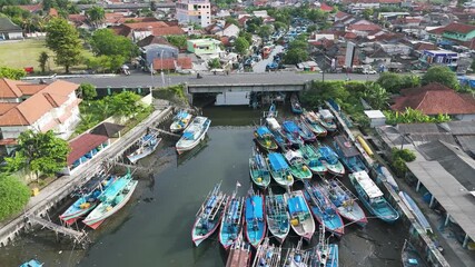 Aerial footage of multiple fishing boats moored along a narrow urban river in a coastal town.