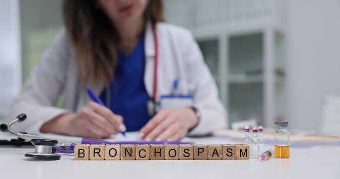 Wooden blocks on medical desk spell word Bronchospasm beside ampoules and stethoscope. Woman doctor writes asthma note adjusting treatment plan