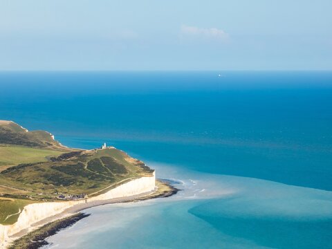 Aerial view of the iconic white cliffs meeting the vast expanse of the turquoise sea, crowned by the Belle Tout Lighthouse, Eastbourne, England, United Kingdom.
