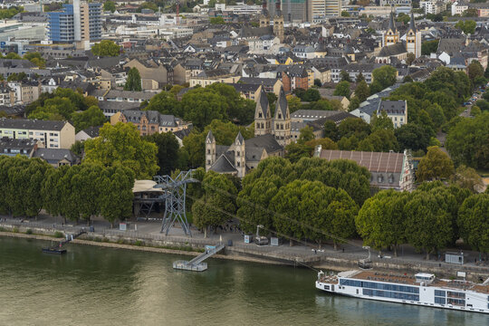 Aerial view of the Basilica of St. Castor nestled among lush green trees near the riverbank, with a cable car station in the foreground, Koblenz, Rhineland-Palatinate, Germany.