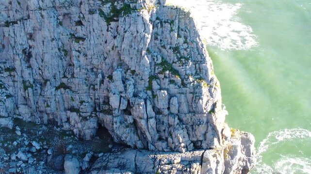 Sideways Aerial Tilting Up to Reveal Beach Along Gower Coast with Crumbling Rockface. Dramatic Drone Clip of Natural Welsh Coastline. Popular Scenic Tourist Destination.