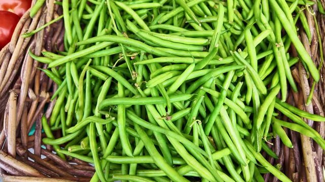 Top-down close-up view of fresh green beans piled in a rustic wicker basket. Raw organic string beans display at a farmers market. Ideal for healthy eating and vegan food concepts