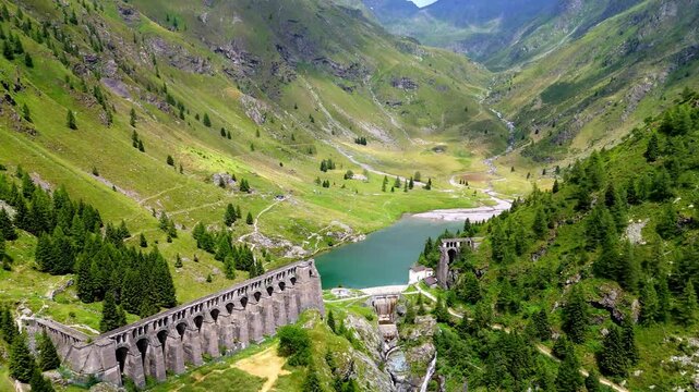 Aerial drone view of Gleno Dam in Val di Scalve, Italian Dolomites and Alpi Orobie. The historic dam is nestled among rugged alpine peaks and lush valleys, creating a dramatic and scenic landscape