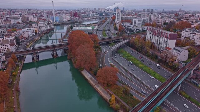 Aerial drone view of highway traffic and a railway bridge over the Marne River near Paris. Autumn urban landscape featuring the Ivry incinerator skyline and transport infrastructure, France