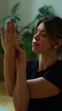 Extreme close-up vertical shot of a woman with her eyes closed or gazing down, performing the arm position of Garudasana (Eagle Pose) or Gomukhasana (Cow Face Pose) for a shoulder and triceps stretch 