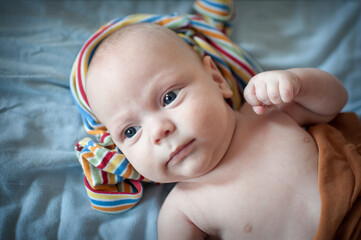 Newborn baby with blue eyes is lying on a soft blue blanket. A striped blanket is wrapped around the baby's head, and an orange blanket covers part of the baby's body.