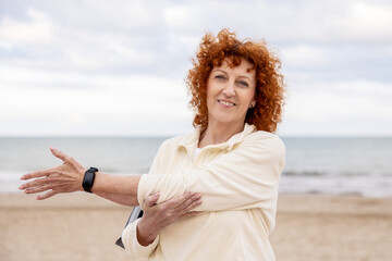 Smiling senior woman stretching her arm by the beach before exercising