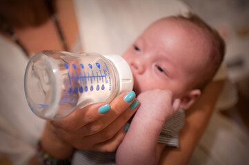 A young infant is being held and fed a bottle by their Mother. The baby is drinking from the bottle, and the Mother is holding the bottle securely.