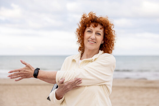 Smiling senior woman stretching her arm by the beach before exercising - Powered by Adobe