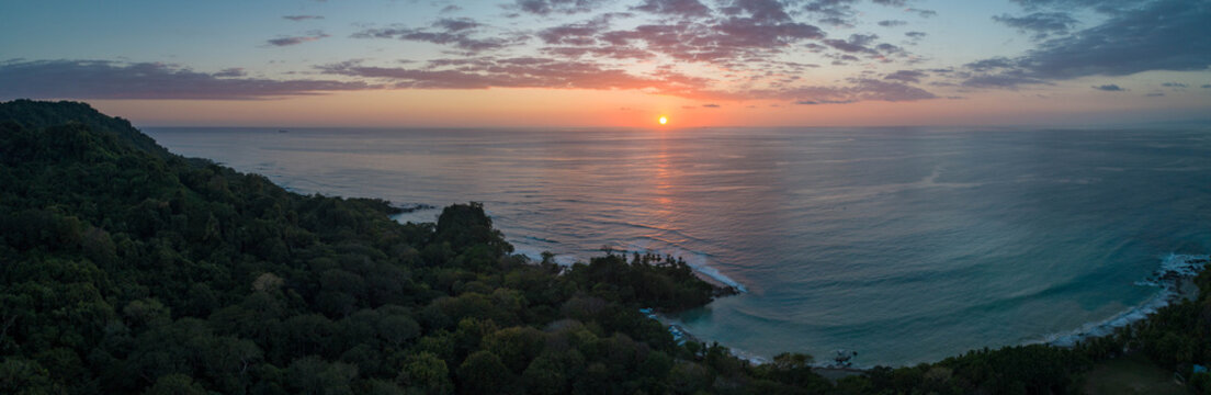 Aerial view of the sun dipping below the horizon, casting a warm glow over the Oregon Coast's lush forests and tranquil waters, Oregon Coast, Oregon, United States.