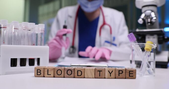 Text Blood Type on wooden blocks near test tubes of blood samples and doctor in hospital. Female assistant conducts research at table in medical lab