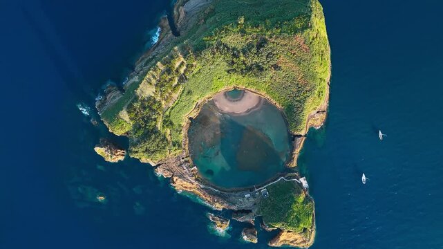 Natural crater pool inside volcanic islet in Azores with contrasting deep ocean and bright lagoon colors, drone footage