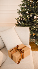 Christmas present box with bow in couch over xmas tree and glowing light at background close up. Winter holiday season. Celebration.