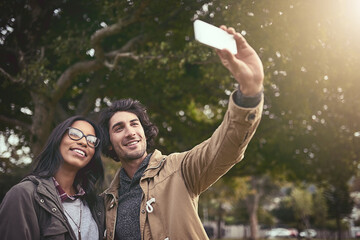 Fototapeta premium Couple, selfie and smile with love in park with care, bonding and adventure in spring on holiday. Interracial people, man and woman with hug, photography or memory on social network on app in Toronto