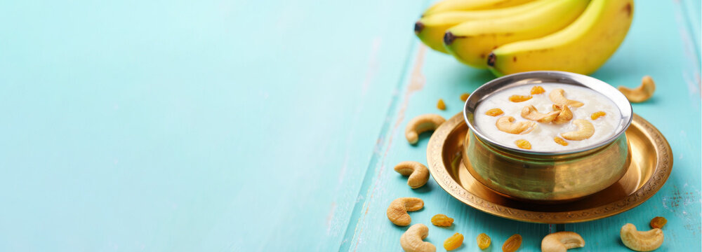Sweet pongal with cashew and raisins in brass bowl, South Indian festive food with bananas, harvest celebration, traditional offering, wide banner with copy space, Pongal Sankranti background