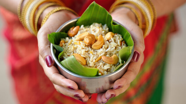 Traditional pongal offering in banana leaf bowl, steaming rice chakkara pongal with roasted cashews, woman's hands with bangles, pattu pavadai veshti, harvest festival rituals, kolam design