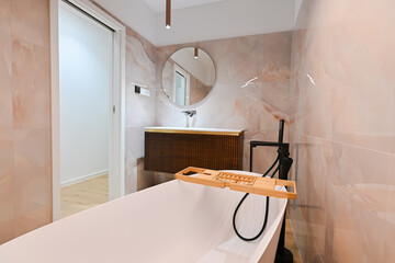 Luxurious modern bathroom featuring a sleek freestanding bathtub with a caddy, elegant vanity with...