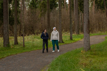 Two women walking together in a park, one wearing a headscarf after cancer therapy. They enjoy clean forest air and gentle conversation