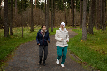 Bald woman with cancer and friend jogging in park, concept of recovery, health, and active lifestyle after treatment.