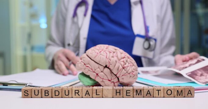 Doctor writes detailed treatment stages for patient. Wooden blocks forming term Subdural Hematoma stand neatly arranged near anatomical brain model