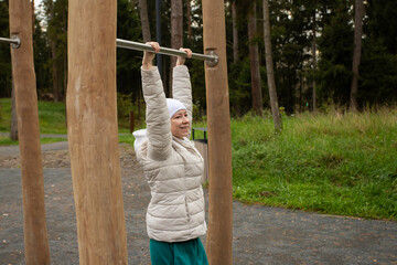 Bald female patient stretching body on outdoor workout area, concept of cancer therapy, balance, and strength.