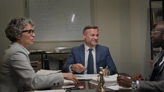 Medium zoom shot of mature Caucasian male senior law firm partner shaking hands with diverse colleagues at team meeting, thanking for ideas and contributions while developing case strategy together