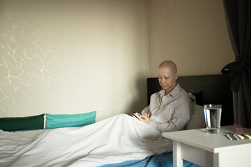Cancer patient with smartphone in bed, woman after chemotherapy resting under blanket, checking medical information online, communication with doctor by telemedicine, remote support during cancer