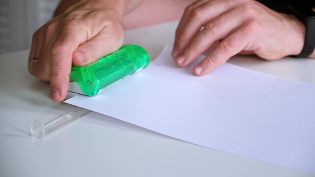 Punching of sheet. A man punches a paper with a hole punch creating a pattern along the edge. Office supplies. School stationery. High quality 4k footage.