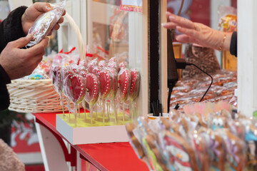 A holiday market stall selling heart-shaped gingerbread cookies and colorful lollipops, packaged in clear wraps for festive gifts.