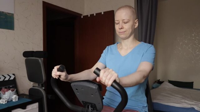 Bald cancer patient in sportswear exercising on stationary bike in bedroom, home physiotherapy and cardiac rehabilitation, low impact training for fatigue and weakness