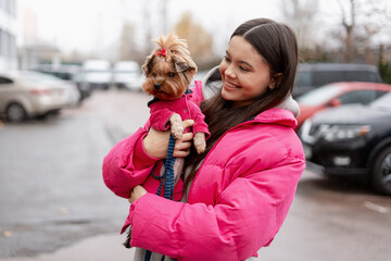 Woman smiling holding Yorkshire Terrier puppy wearing pink jacket outdoors